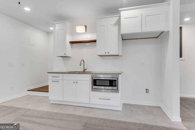 kitchen with backsplash, light colored carpet, sink, white cabinets, and stainless steel microwave