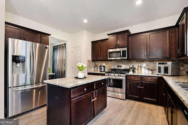 kitchen featuring backsplash, stainless steel appliances, light stone counters, and light hardwood / wood-style floors