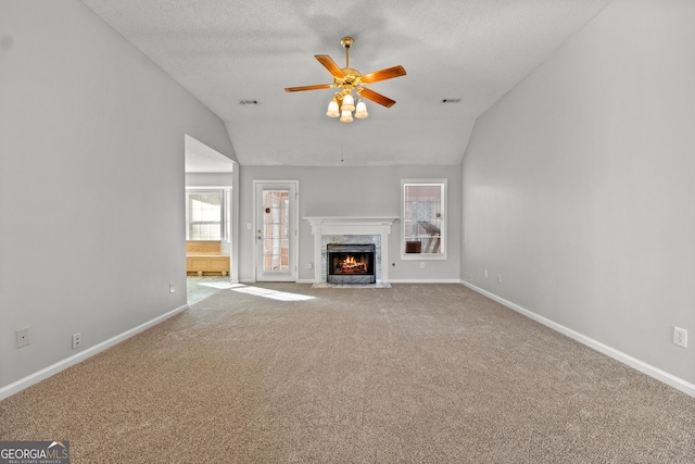 unfurnished living room with ceiling fan, a textured ceiling, vaulted ceiling, a fireplace, and carpet