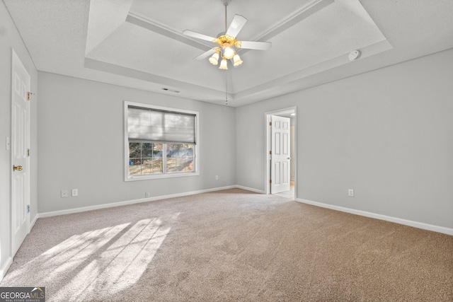 empty room featuring ceiling fan, a raised ceiling, and light carpet