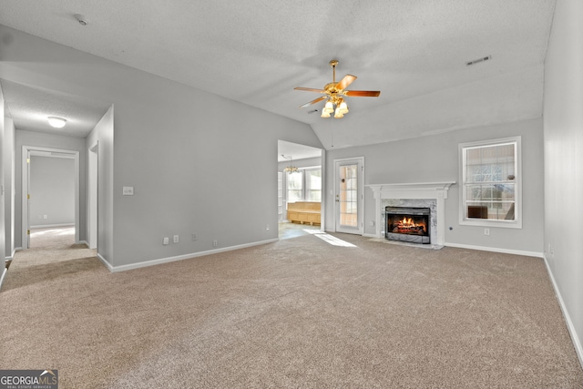 unfurnished living room with vaulted ceiling, ceiling fan, a textured ceiling, a fireplace, and light colored carpet