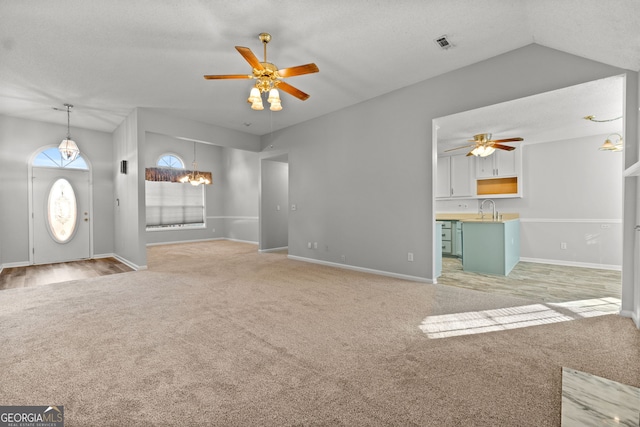 unfurnished living room featuring vaulted ceiling, sink, and ceiling fan with notable chandelier