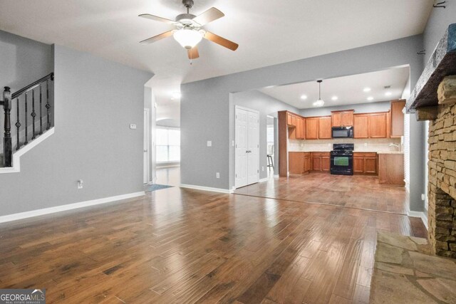 living room with a healthy amount of sunlight, a stone fireplace, ceiling fan, and dark wood-type flooring