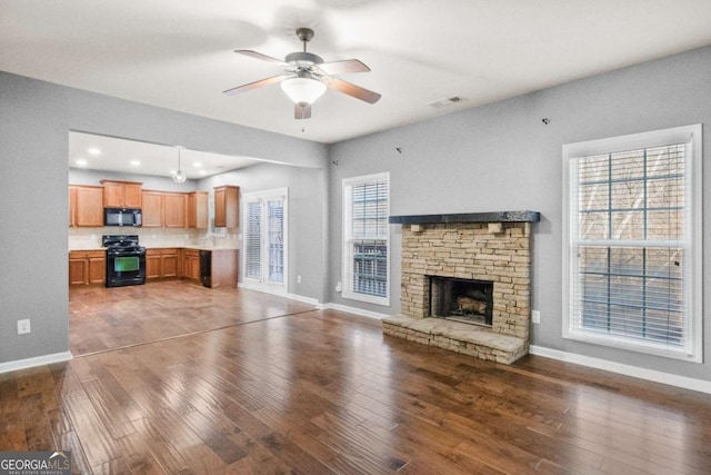 unfurnished living room with a stone fireplace, ceiling fan, and dark hardwood / wood-style flooring