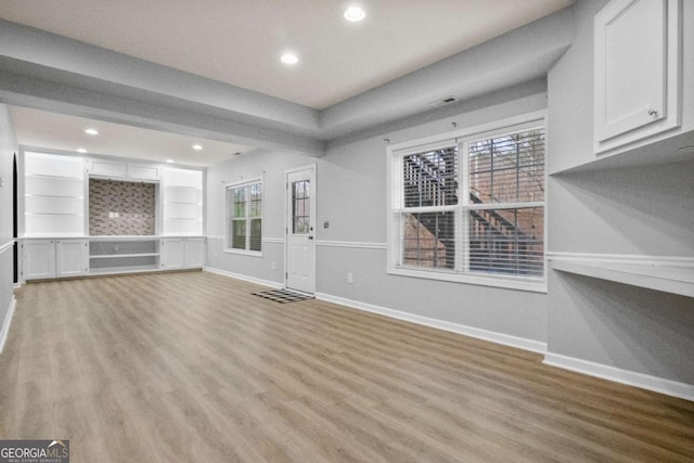 unfurnished living room with built in shelves and light hardwood / wood-style floors