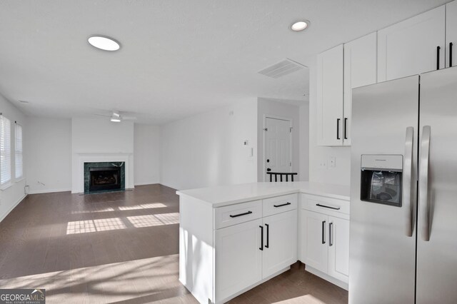 kitchen with dark wood-type flooring, kitchen peninsula, stainless steel fridge with ice dispenser, a premium fireplace, and white cabinetry