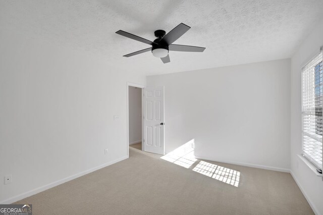 carpeted empty room with a textured ceiling, a wealth of natural light, and ceiling fan