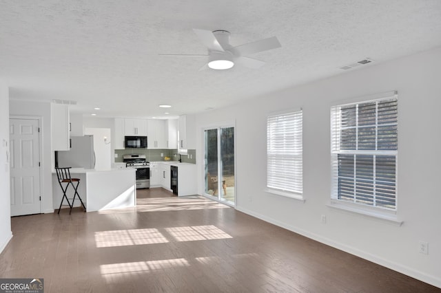 unfurnished living room featuring ceiling fan, dark wood-type flooring, and a textured ceiling