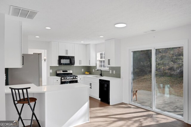 kitchen featuring backsplash, black appliances, sink, kitchen peninsula, and white cabinetry