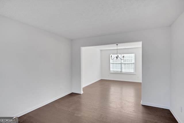 empty room with dark hardwood / wood-style flooring, a textured ceiling, and an inviting chandelier