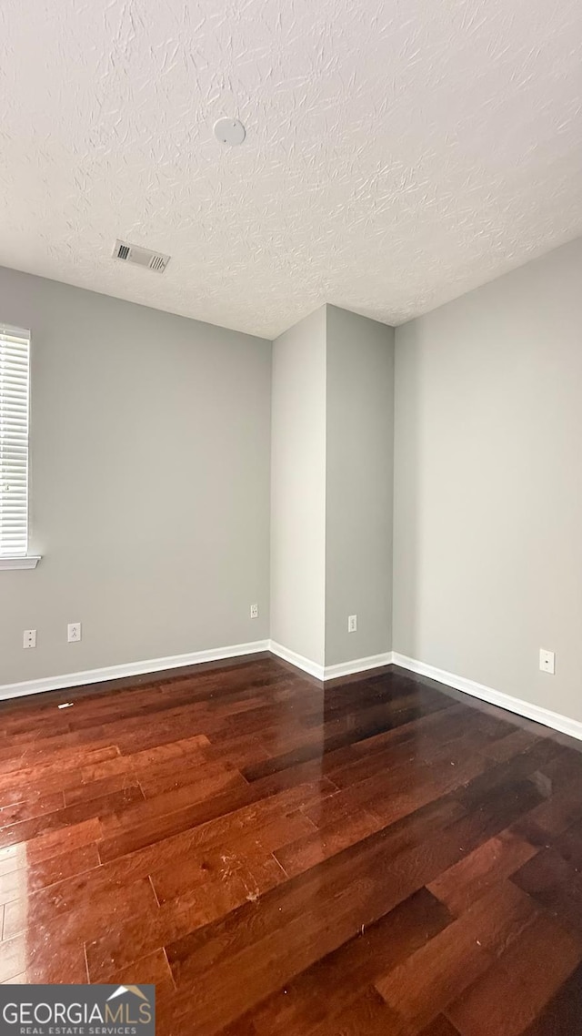 empty room with a textured ceiling and dark hardwood / wood-style floors