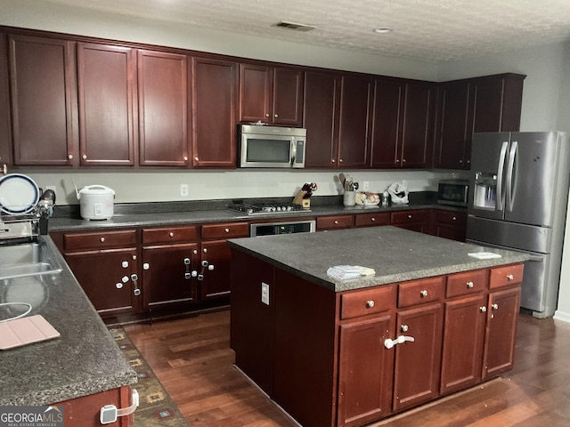 kitchen with a textured ceiling, dark hardwood / wood-style floors, a kitchen island, and stainless steel appliances