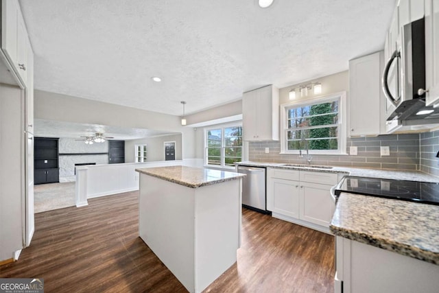 kitchen featuring white cabinets, stainless steel appliances, a kitchen island, and light stone counters