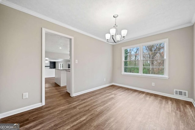 empty room with a textured ceiling, a notable chandelier, ornamental molding, and dark wood-type flooring