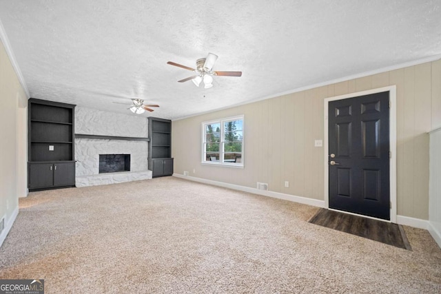 unfurnished living room featuring built in shelves, a stone fireplace, carpet, and a textured ceiling