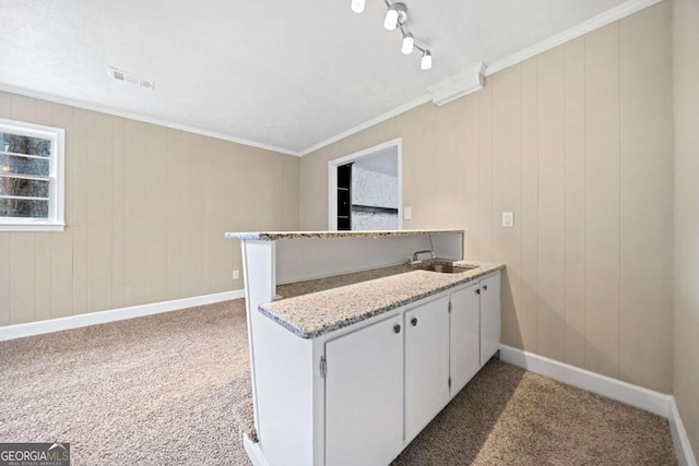 kitchen with white cabinets, dark colored carpet, sink, ornamental molding, and kitchen peninsula