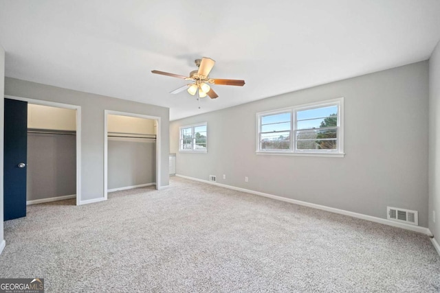 unfurnished bedroom with ceiling fan, carpet floors, and two closets