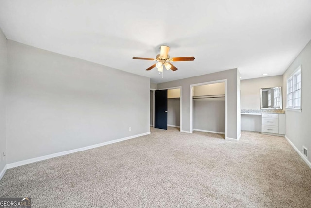 unfurnished bedroom featuring ceiling fan, built in desk, light carpet, and two closets