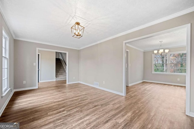 spare room with a chandelier, a textured ceiling, hardwood / wood-style flooring, and crown molding