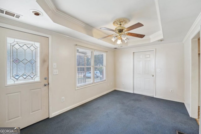 foyer with a raised ceiling, ceiling fan, crown molding, and dark colored carpet