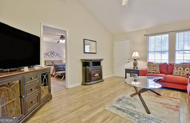 living room featuring ceiling fan, vaulted ceiling, a wood stove, and light hardwood / wood-style flooring