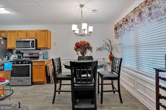 kitchen with pendant lighting, light hardwood / wood-style floors, appliances with stainless steel finishes, and a chandelier