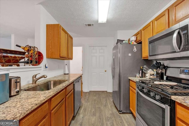 kitchen with appliances with stainless steel finishes, light wood-type flooring, a textured ceiling, and sink