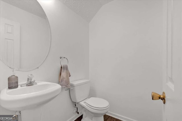 bathroom featuring sink, toilet, lofted ceiling, and a textured ceiling