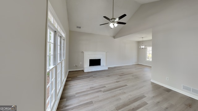 unfurnished living room featuring ceiling fan with notable chandelier, light wood-type flooring, high vaulted ceiling, and a brick fireplace