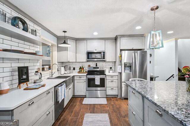 kitchen with gray cabinetry, hanging light fixtures, stainless steel appliances, tasteful backsplash, and light stone counters