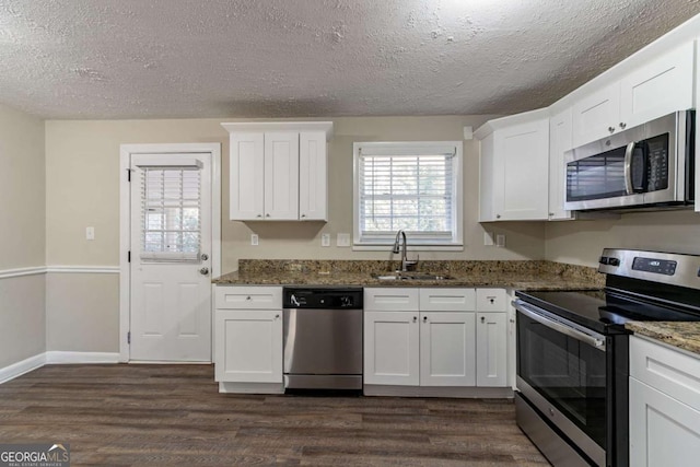 kitchen featuring stainless steel appliances, white cabinetry, dark stone countertops, and sink