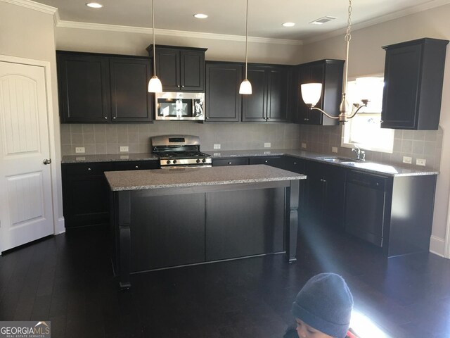 kitchen with light stone counters, appliances with stainless steel finishes, decorative light fixtures, a kitchen island, and dark hardwood / wood-style flooring