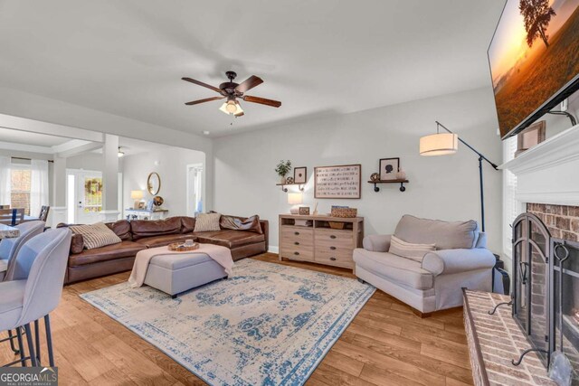 living area featuring a brick fireplace, light wood finished floors, and a ceiling fan