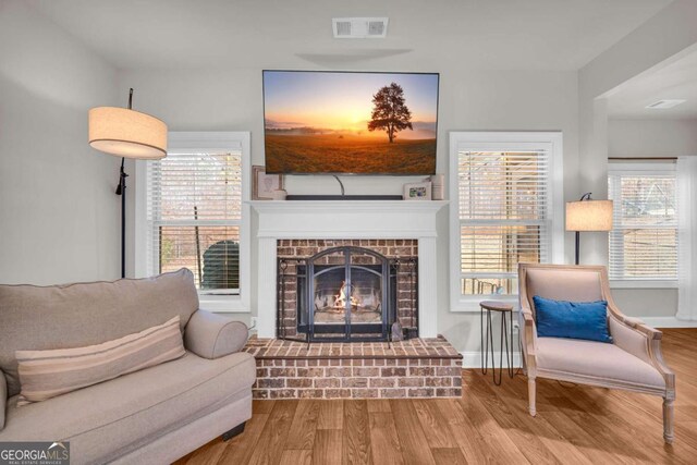 living area featuring a wealth of natural light, a fireplace, visible vents, and wood finished floors