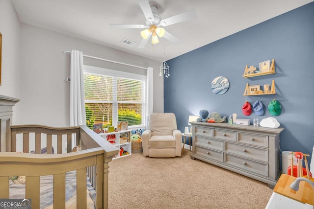 carpeted bedroom featuring a nursery area, ceiling fan, and visible vents