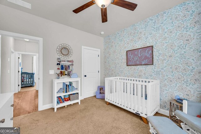 bedroom with visible vents, carpet flooring, a nursery area, baseboards, and wallpapered walls