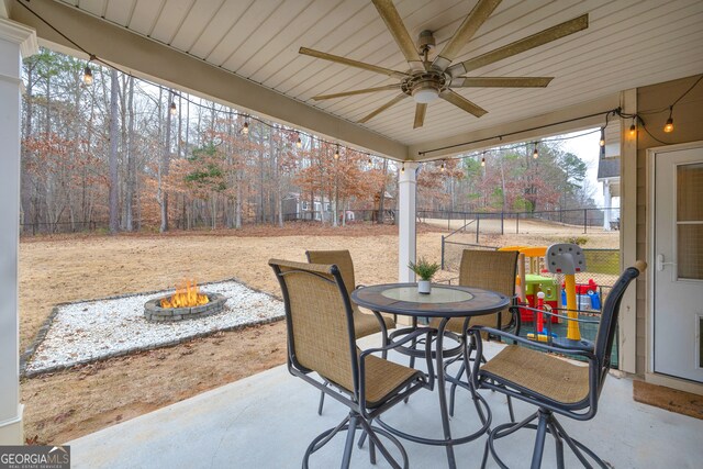 view of patio with a fire pit, ceiling fan, outdoor dining area, and fence