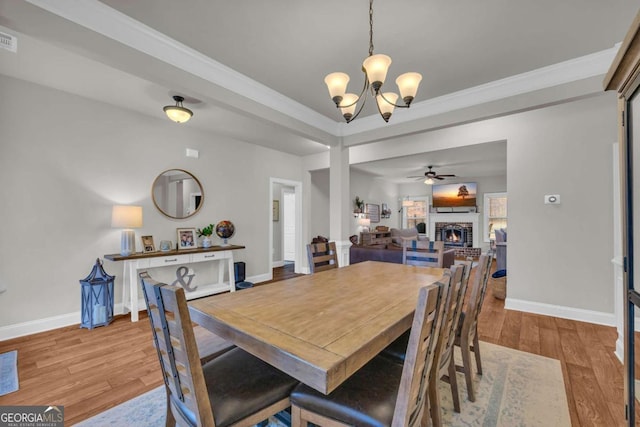 dining room with crown molding, a fireplace, wood finished floors, baseboards, and ceiling fan with notable chandelier