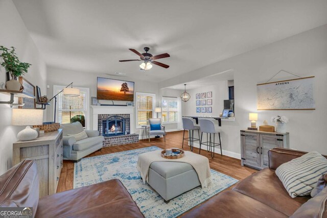 living area featuring a brick fireplace, ceiling fan, baseboards, and wood finished floors