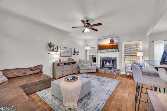 living room featuring baseboards, a fireplace, a ceiling fan, and wood finished floors