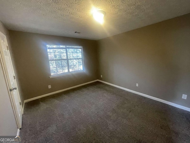 spare room with a textured ceiling and dark colored carpet