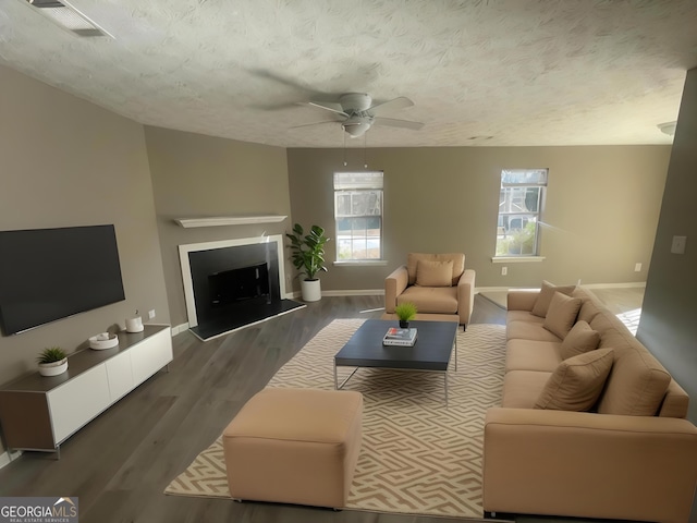 living room featuring ceiling fan, dark wood-type flooring, and a textured ceiling