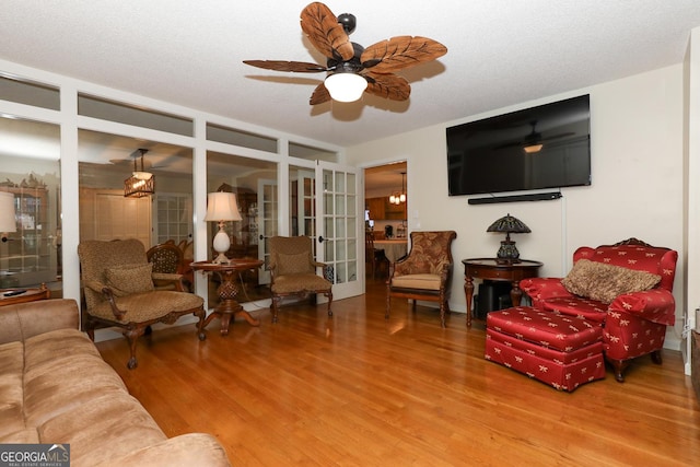 living room featuring a textured ceiling, french doors, wood-type flooring, and ceiling fan with notable chandelier