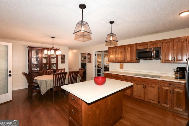 kitchen with black electric stovetop, decorative light fixtures, a kitchen island, and dark wood-type flooring