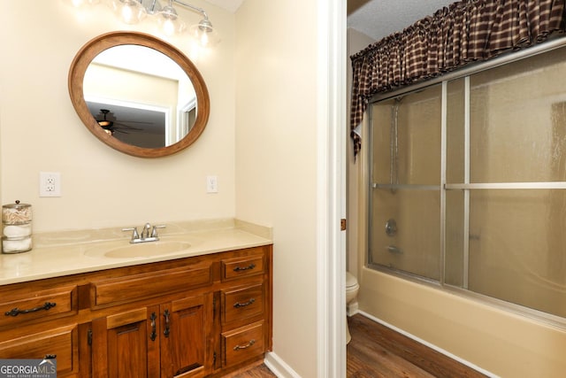 full bathroom featuring bath / shower combo with glass door, vanity, ceiling fan, wood-type flooring, and toilet