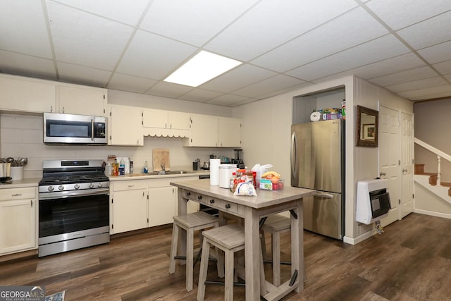 kitchen featuring a drop ceiling, dark wood-type flooring, cream cabinets, stainless steel appliances, and heating unit