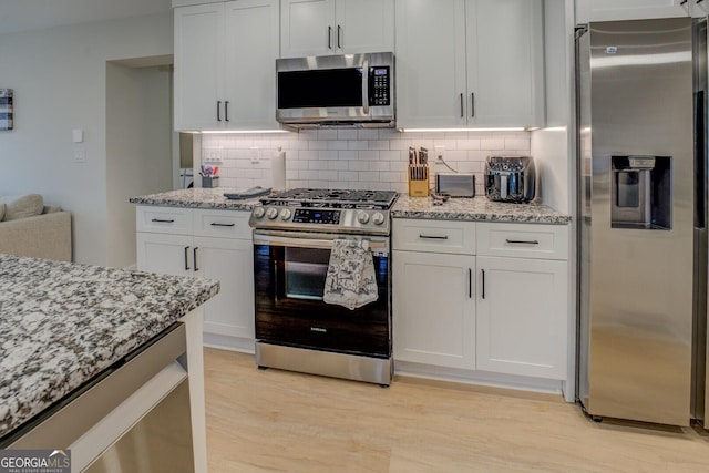 kitchen featuring white cabinets, light stone counters, stainless steel appliances, and tasteful backsplash