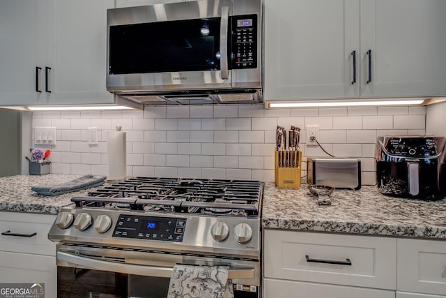 kitchen with white cabinets, decorative backsplash, light stone counters, and stainless steel appliances