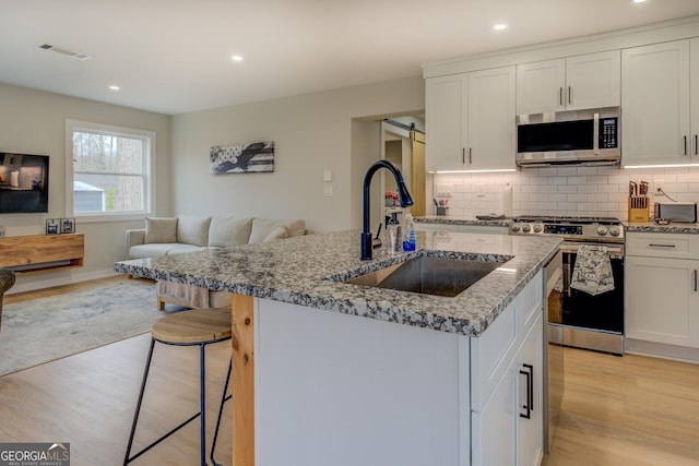 kitchen featuring light stone countertops, stainless steel appliances, sink, a center island with sink, and white cabinets