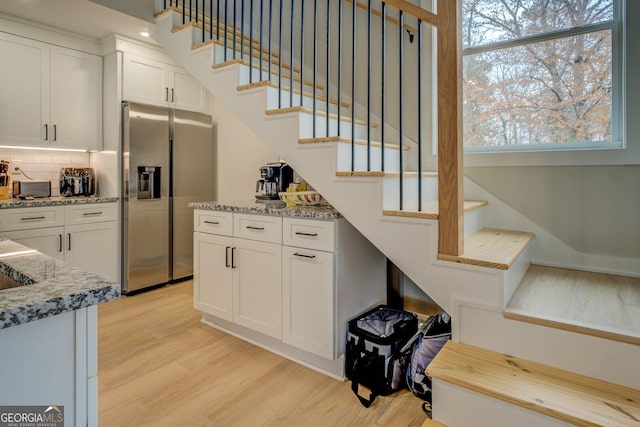 kitchen featuring backsplash, stainless steel refrigerator with ice dispenser, light hardwood / wood-style floors, light stone counters, and white cabinetry